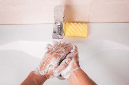 Man washing hands with soap under faucet in bathroom