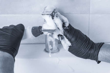 Hands of man in protective gloves cleaning tap at bathroom. Toned image