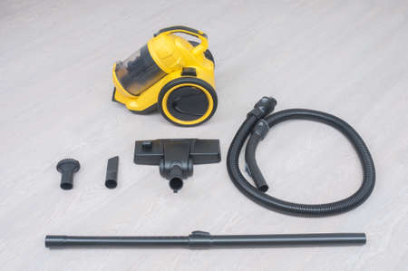 Yellow vacuum cleaner with hose and brushes on wooden floorの写真素材
