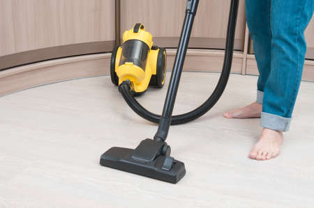 Barefoot man using vacuum cleaner for chore in a roomの写真素材
