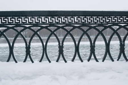 Metal fence at embankment of frozen river in a winter parklandの写真素材