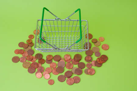 Pile of euro cent coins and metal shopping basket on green background