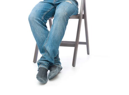 Legs of man in jeans and socks sitting on chair on white backgroundの写真素材