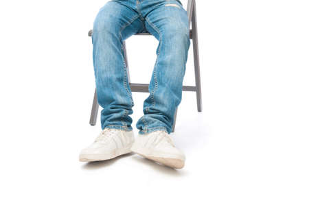 Legs of man with jeans and sneakers sitting on chair on white backgroundの写真素材
