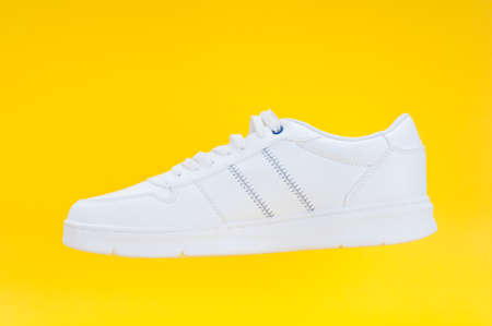 Single white sport sneaker close up on yellow backgroundの写真素材