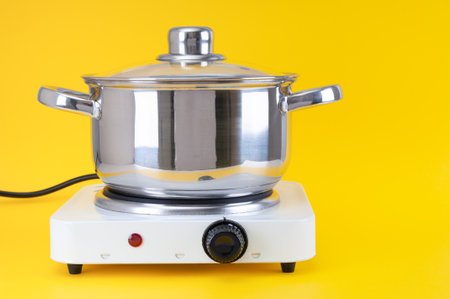 Stainless saucepan on portable electric stove close up on yellow backgroundの写真素材