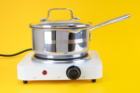 Stainless saucepan on portable electric stove close up on yellow backgroundの写真素材