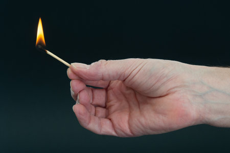 Burning matchstick in hand on a dark backgroundの写真素材