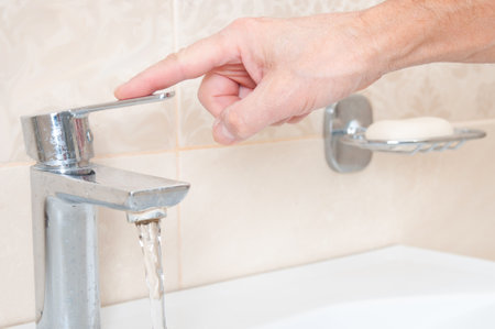 Man's hand turns off the water in the tapの写真素材