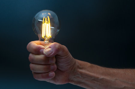 Glowing light bulb in man's hand on a dark backgroundの写真素材