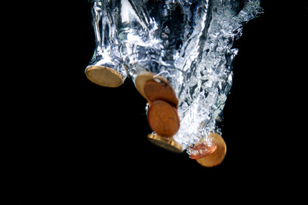 Euro cent coins fall with a splash into water on black background