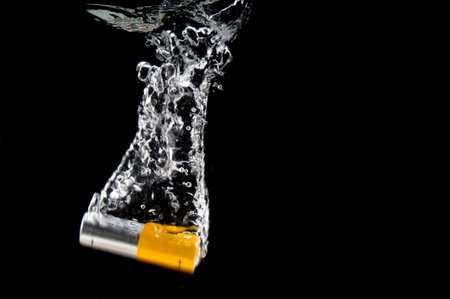 Alkaline AA battery falls with a splash into water on black backgroundの写真素材