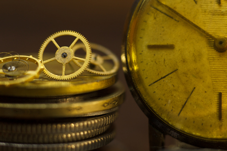 Time is money! Close-up of stacked coins, an old wristwatch and some small metal gears with dark...