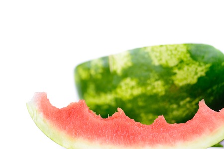 Some of the watermelon was already eaten. From a juicy slice, someone bitten a bite. In the background half of the melon is visible on a white background.の写真素材