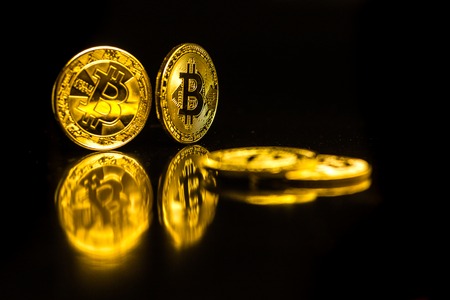 Bitcoin coins are laid on a reflecting surface on a black background and are mounted on their edges.の写真素材
