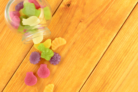 colored gummy fruit candy spilled on a orange wooden table.の写真素材