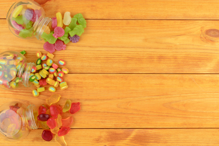 colored gummy fruit candy spilled on a orange wooden table.の写真素材