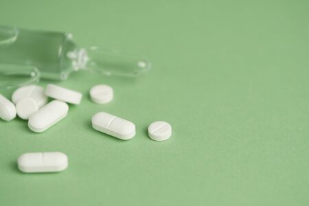 White medical pills and medical preparations in with bottles, glass ampoues,close-up on green...