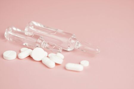 White medical pills and medical preparations in with bottles, glass ampoues,close-up on pink...