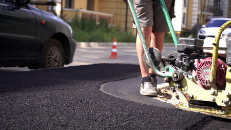 Close-up,working men shoveling black gravel for laying asphalt on the road and sidewalk,working outdoors,hard work.Laying asphalt with a manual vibratory rollerの写真素材