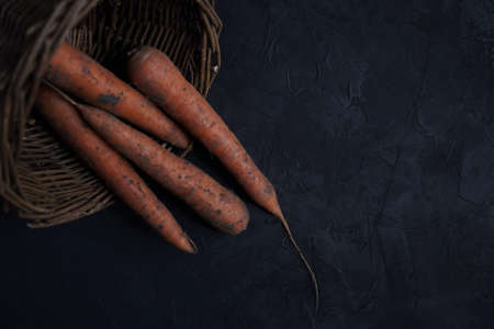 Fresh carrots lie in a basket on a black background, collected in a vegetable garden.View from above, close-upの写真素材