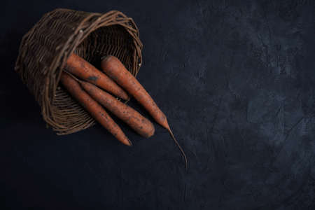 Fresh carrots lie in a basket on a black background, collected in a vegetable garden.View from aboveの写真素材