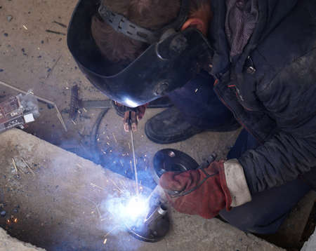 Close-up welder working with electrode at semi-automatic arc welding in manufacture production...