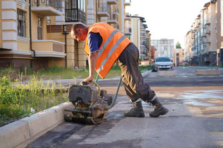 Worker pushes a manual roller for asphalt paving of the sidewalk .. Road works close-up.のeditorial素材