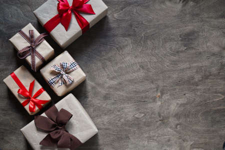 Many gift boxes wrapped in brown paper and tied with different ribbons on a wooden background, top view, copy space. Christmas and New Year conceptの写真素材