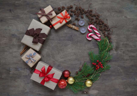 Christmas wreath made of gift boxes, Christmas tree branches, pine cones, Christmas toy balls, candles, lollipops and cinnamon on brown background top view. Concept of Christmas and New Year cardの写真素材