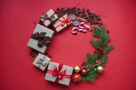Christmas wreath made of gift boxes, Christmas tree branches, pine cones, Christmas toy balls, candles, lollipops and cinnamon on red background top view. Concept of Christmas and New Year cardの写真素材