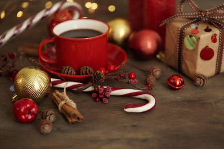 Christmas decorations.Red cup with coffee, gift box, Christmas candies, balls, cones and cinnamon on a wooden background, selective focus. Christmas and New Year concept.の写真素材