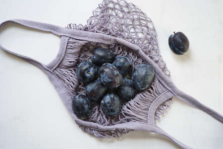 Blue plum in a string bag on a white marble background, flat lay, top view. Concept zero waste.の写真素材