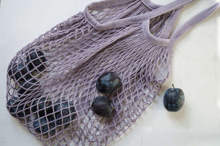 Blue plum in a string bag on a white marble background, flat lay, top view. Concept zero waste.の写真素材