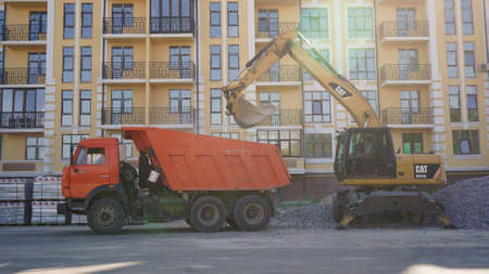 Yellow CAT excavator loader works on a construction site with gravel. Loading gravel onto a truck. Road construction site. Construction of a parking lot, Kiev, Ukraine 09.02.のeditorial素材