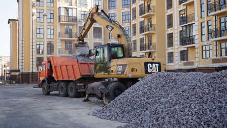 Yellow CAT excavator loader works on a construction site with gravel. Loading gravel onto a truck. Road construction site. Construction of a parking lot, Kiev, Ukraine 09.02.のeditorial素材