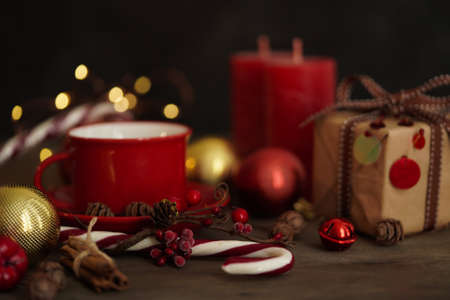 Christmas decorations.Red cup with coffee, gift box, Christmas candies, balls, cones and cinnamon on a wooden background, selective focus. Christmas and New Year concept.の写真素材
