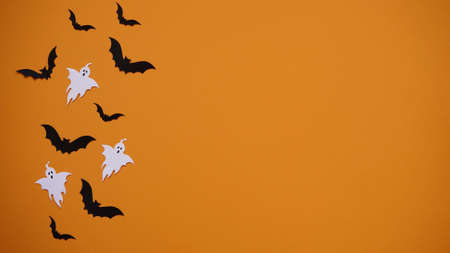 Halloween holiday concept. Black paper bats and ghosts on bright orange background, top view, flat lay, copy spaes. Celebration of the dead.の写真素材