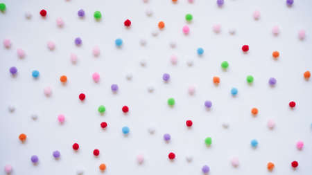 Many small bright colored pom-poms on a white background, top view, flat lay. Background concept for...