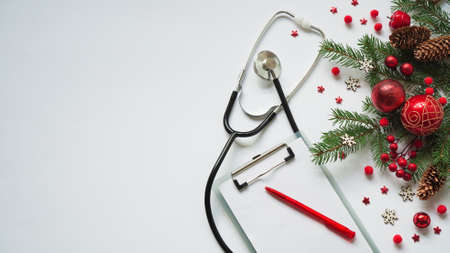 Christmas medical banner fir branches, cones, red balls, snowflakes, stethoscope and tablet on white background top view. Copyspace. Medicine new year flatly.の写真素材
