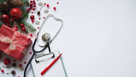 Christmas medical banner gift box, fir branches, cones, red balls, snowflakes, stethoscope and tablet on white background top view. Copyspace. Medicine new year flatly. Doctor writes down the text.の写真素材