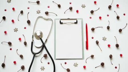 Christmas medical banner cones, red balls, snowflakes, stethoscope and tablet on white background top view. Copyspace. Medicine new year flatly. Doctor writes down the text.の写真素材