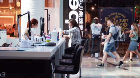 Young woman in medical mask makes manicure in express manicure studio in hall of large shopping...