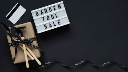 Banner concept for Black Friday celebration, lettering.White board with text GARDEN TOOL SALE, gift box with garden tools, credit card on black background, top view, flat lay, close-up, copy spaceの写真素材