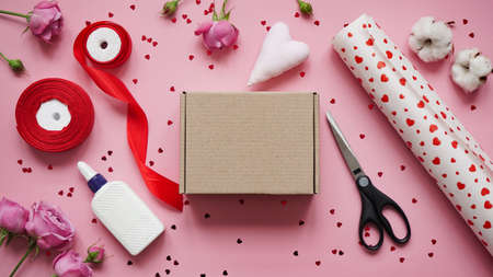 Step 1. Step-by-step instructions for wrapping gifts for Valentine's Day. Woman wraps a gift with wrapping white paper in heart and seals the edges with glue on a pink background top view, flat lay.の写真素材