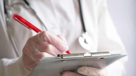 Close-up of a doctor writing a prescription in a medical record on a tablet.