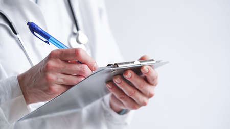 Close-up of a doctor writing a prescription in a medical record on a tablet.