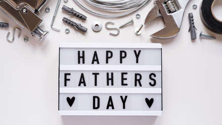 Happy Fathers Day banner concept.Working repair tools upholstery stapler, screwdriver, screws, adjustable wrench, duct tape and light box with Happy Fathers Day text white background, top view, flat lay.の写真素材