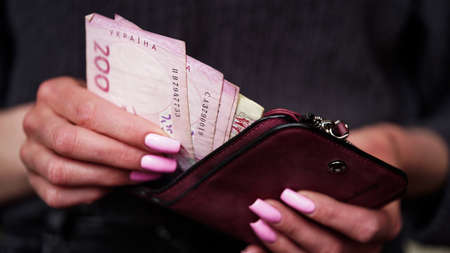 Close-up of female hands take out hryvnia banknotes from a lilac purse, Ukrainian currency. The...