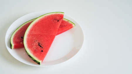 Close-up slices of fresh ripe red watermelon on a plate with a knife on the table on a white background, half of a watermelon. Ripe juicy summer berries, melon season. Macrophotoの写真素材